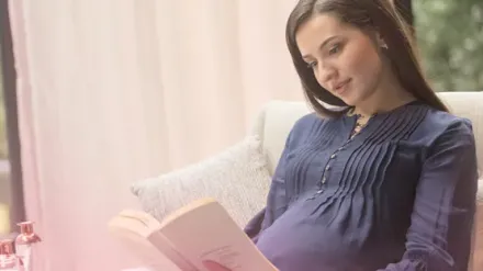 Pregnant woman reading book on pregnancy tips and symptoms