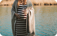 Pregnant lady wearing a horizontal pinstriped flowy dress with a long maternity coat
