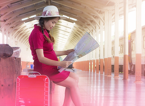 Pregnant woman seated at a train station looking at her travel map with her luggage next to her