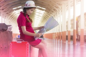Pregnant woman seated at a train station looking at her travel map with her luggage next to her