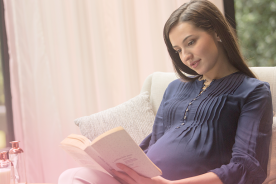 Pregnant woman reading book on pregnancy tips and symptoms