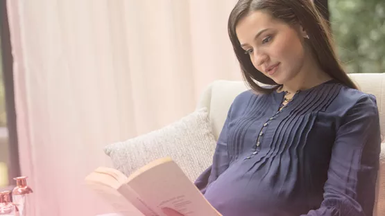 Pregnant woman reading book on pregnancy tips and symptoms