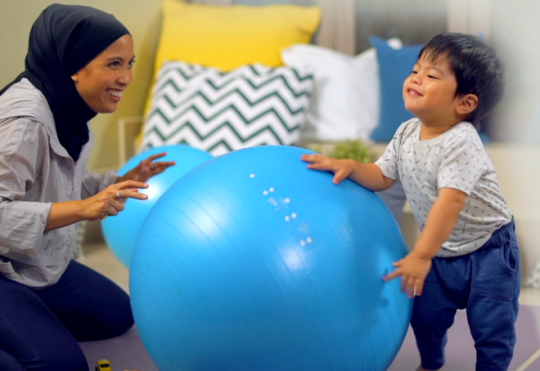 Mother playing blue yoga ball with kid