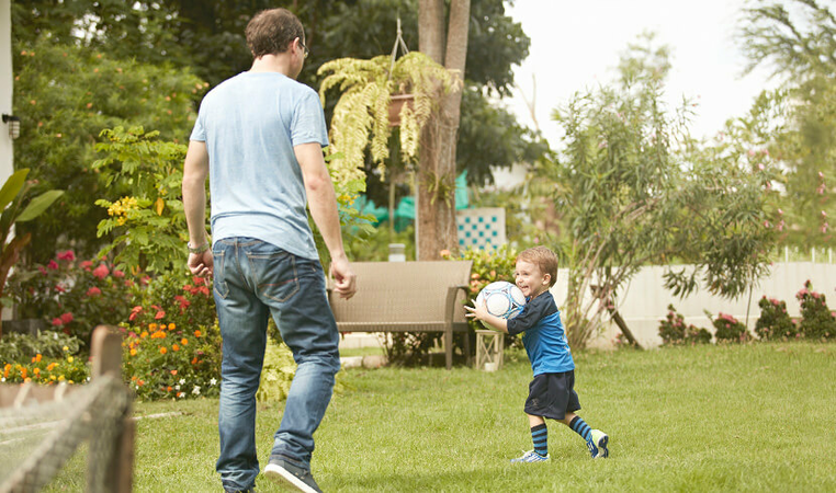 Father playing football with kid in the garden