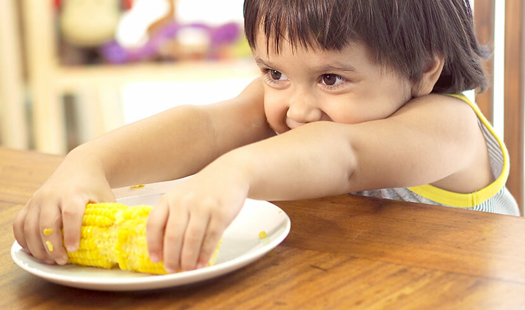 Kid grabbing corn on plate
